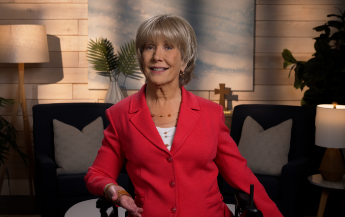 Joni wearing a blazer and smiling for the camera in a cozy living room setup.