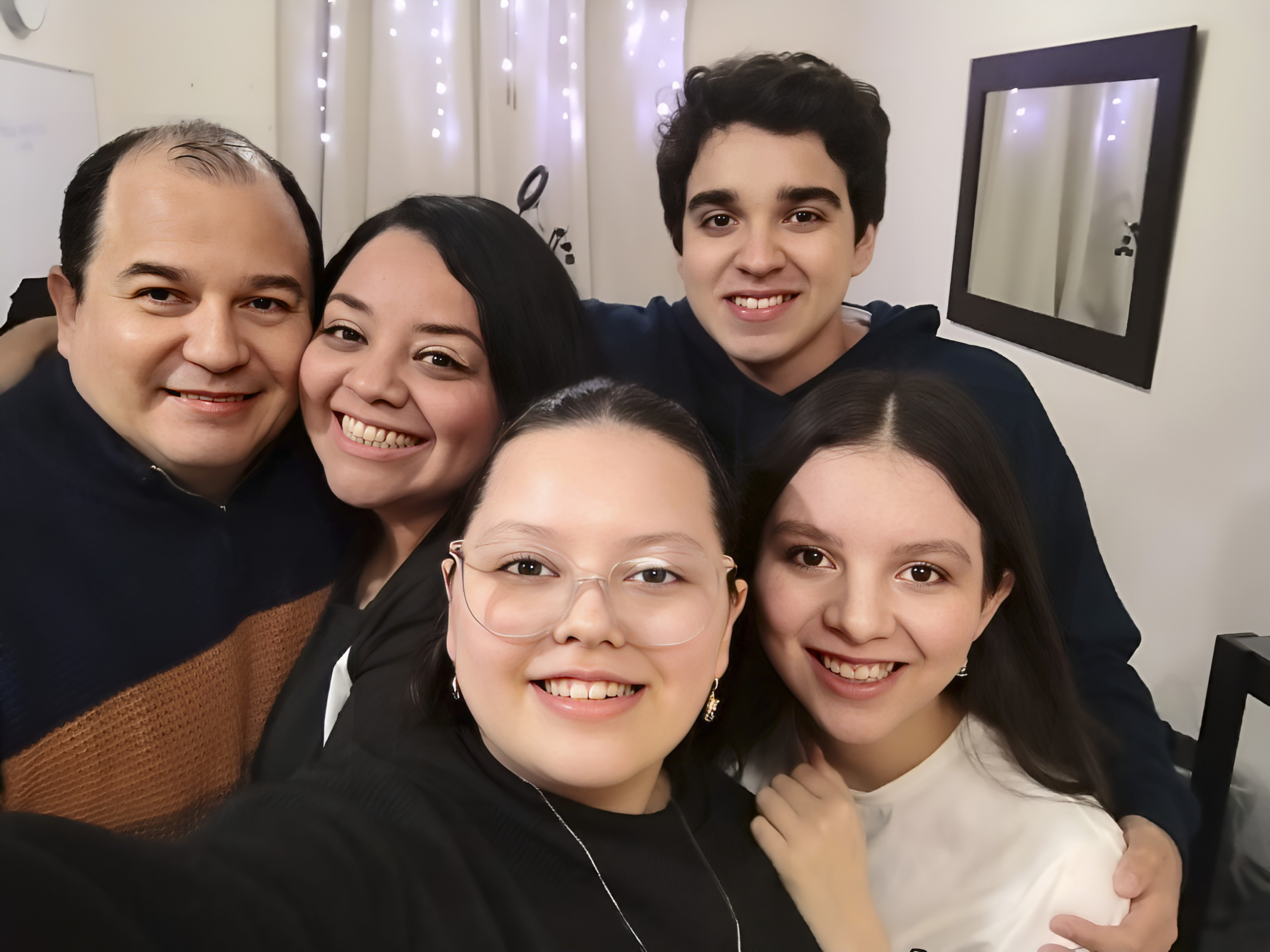 A beautiful selfie of Vianey with her family, all smiling together in a cozy indoor setting with warm lighting and a comfortable atmosphere.