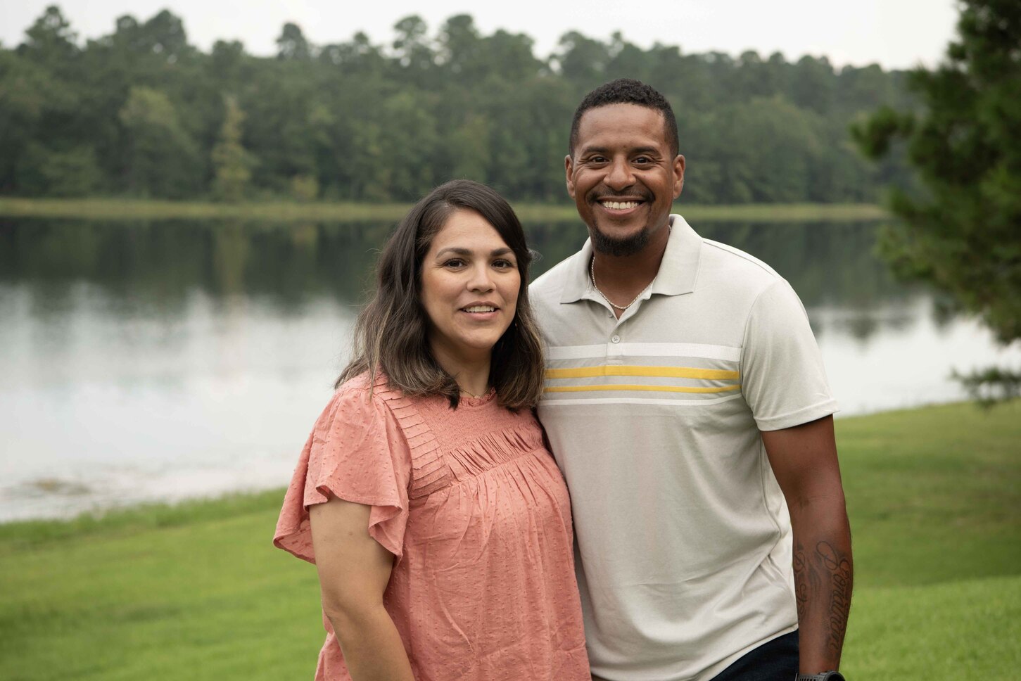 JB next to his wife Melissa, both posing for the camera with a lake in the background.