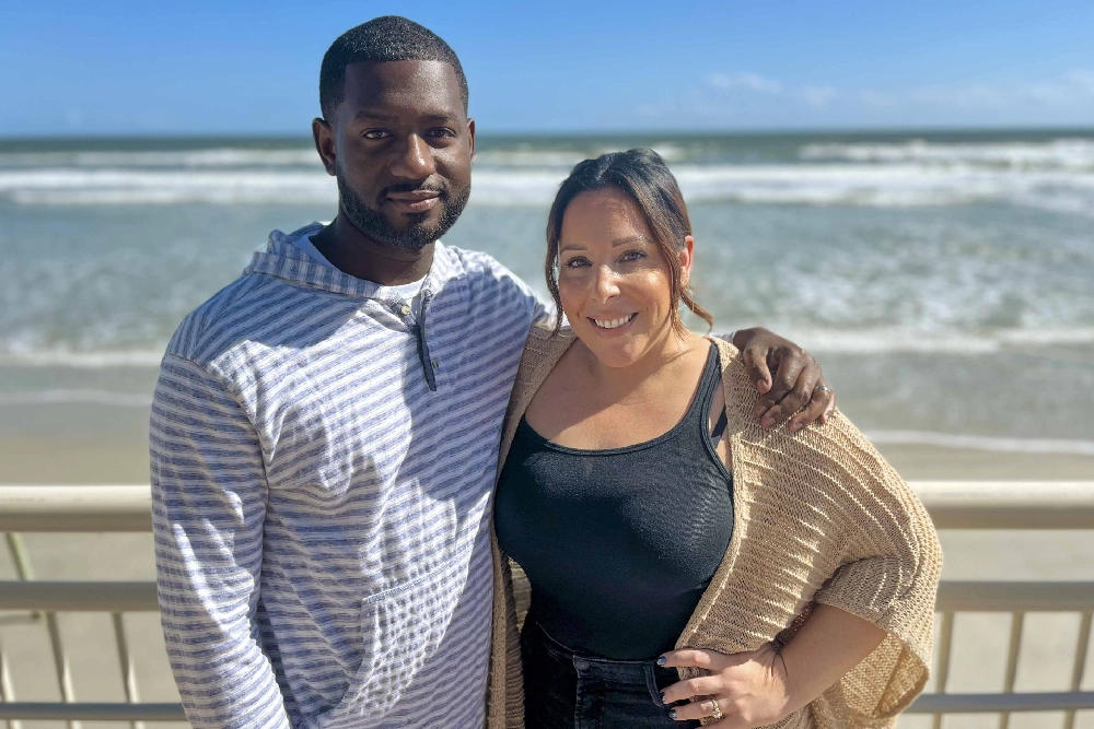 A couple poses for a photo in front of a beach