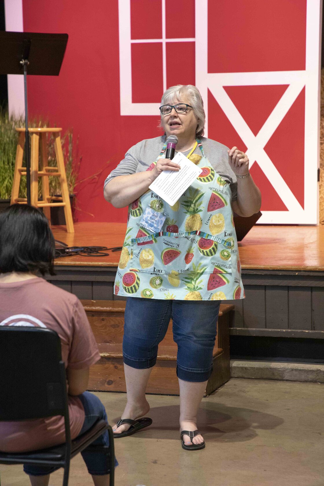 Deb Butcher holding a microphone below the stage, with a barn backdrop.