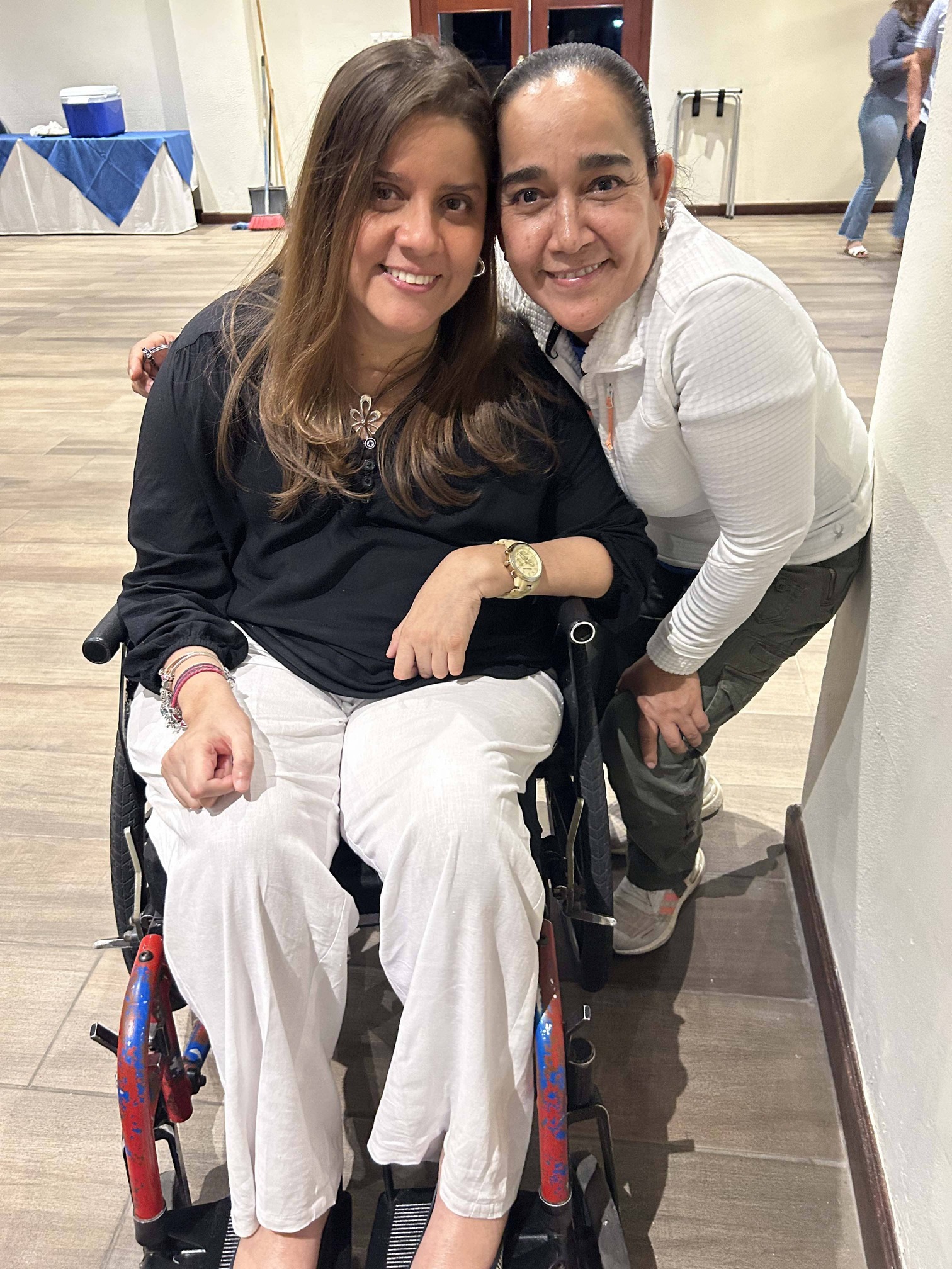 Imelda Cuevas standing next to a woman in a wheelchair, both smiling and posing for the camera.