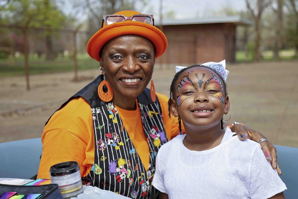 A woman in orange holding a girl with a butterfly painted on her face
