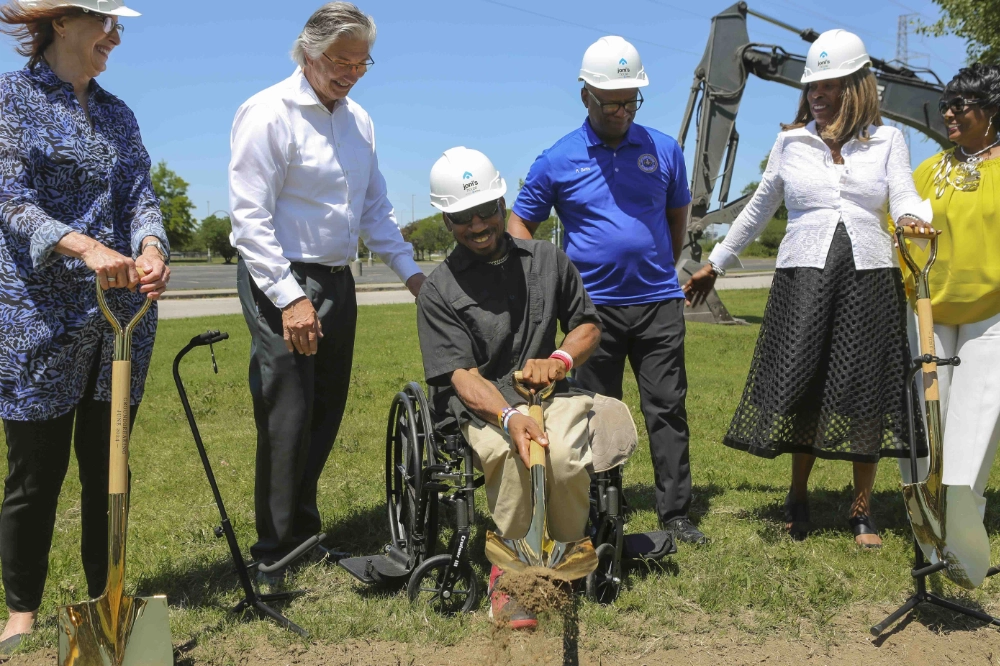 A man in a wheelchair throws a shovel of dirt as people smile and surround him