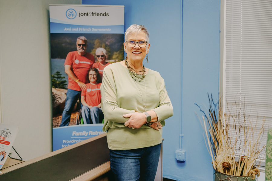 Roberta Dunn standing with her arms crossed, posing for the camera, with a Joni and Friends Family Retreat banner in the background.