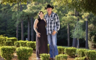 Chet Falkenhainer standing outdoors with his wife, Amy, both smiling and posing for the camera in a beautifully photographed natural setting.