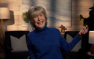 Joni Eareckson Tada smiling, wearing a long-sleeve turtle neck in a cozy living room.