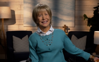 Joni Eareckson Tada smiling, wearing a long-sleeve in a cozy living room.