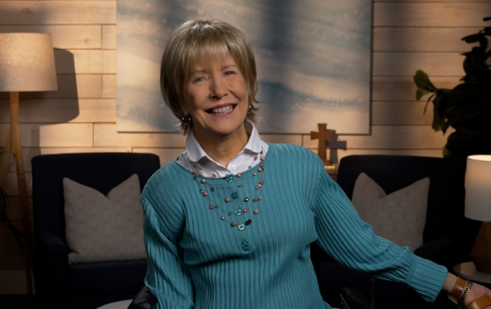 Joni Eareckson Tada smiling, wearing a long-sleeve in a cozy living room.