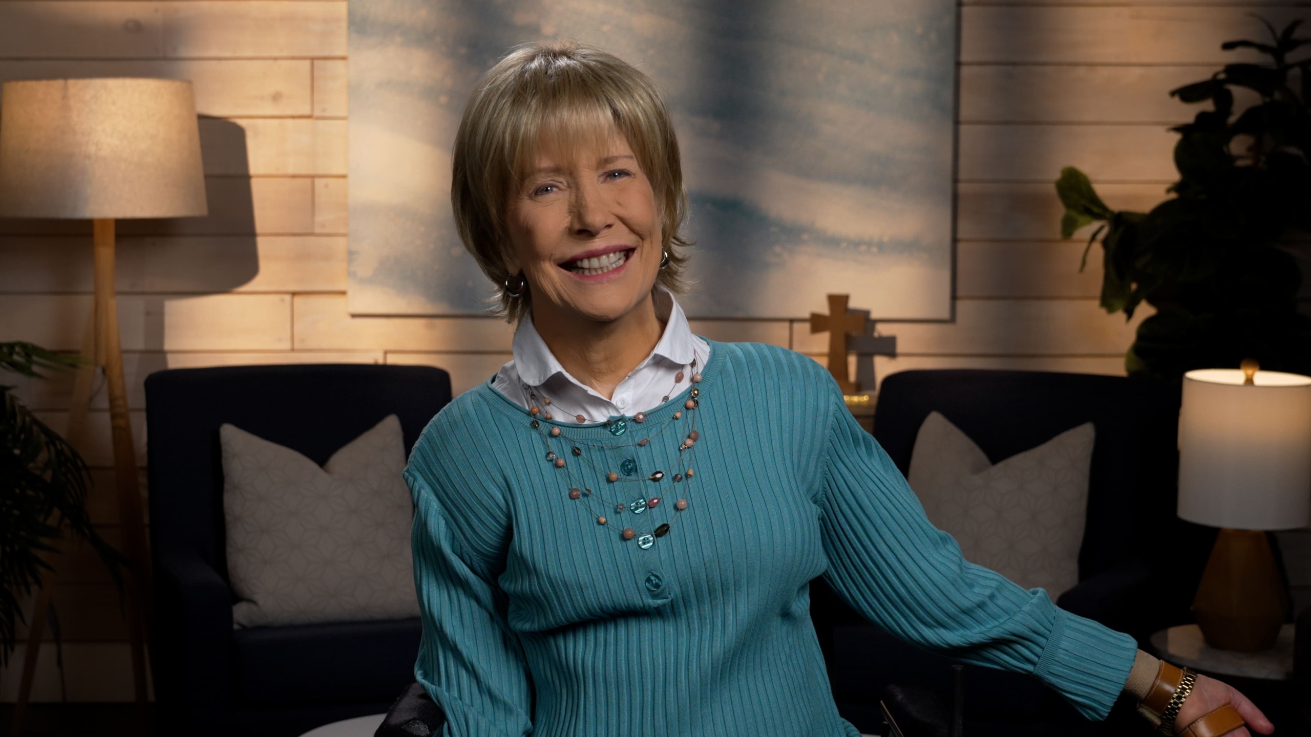 Joni Eareckson Tada smiling, wearing a long-sleeve in a cozy living room.