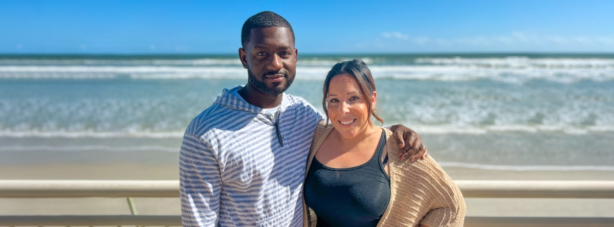 A couple poses for a photo in front of the beach