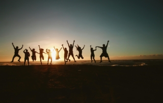 A silhouette of a group of people captured mid-jump on the beach at sunset.