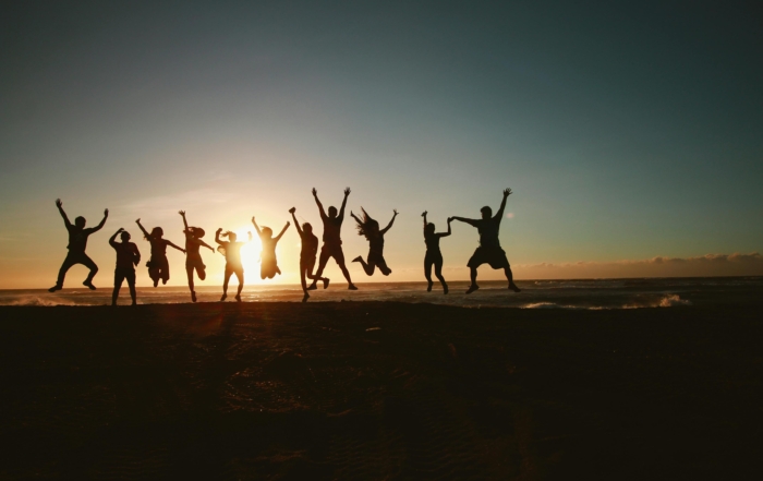 A silhouette of a group of people captured mid-jump on the beach at sunset.
