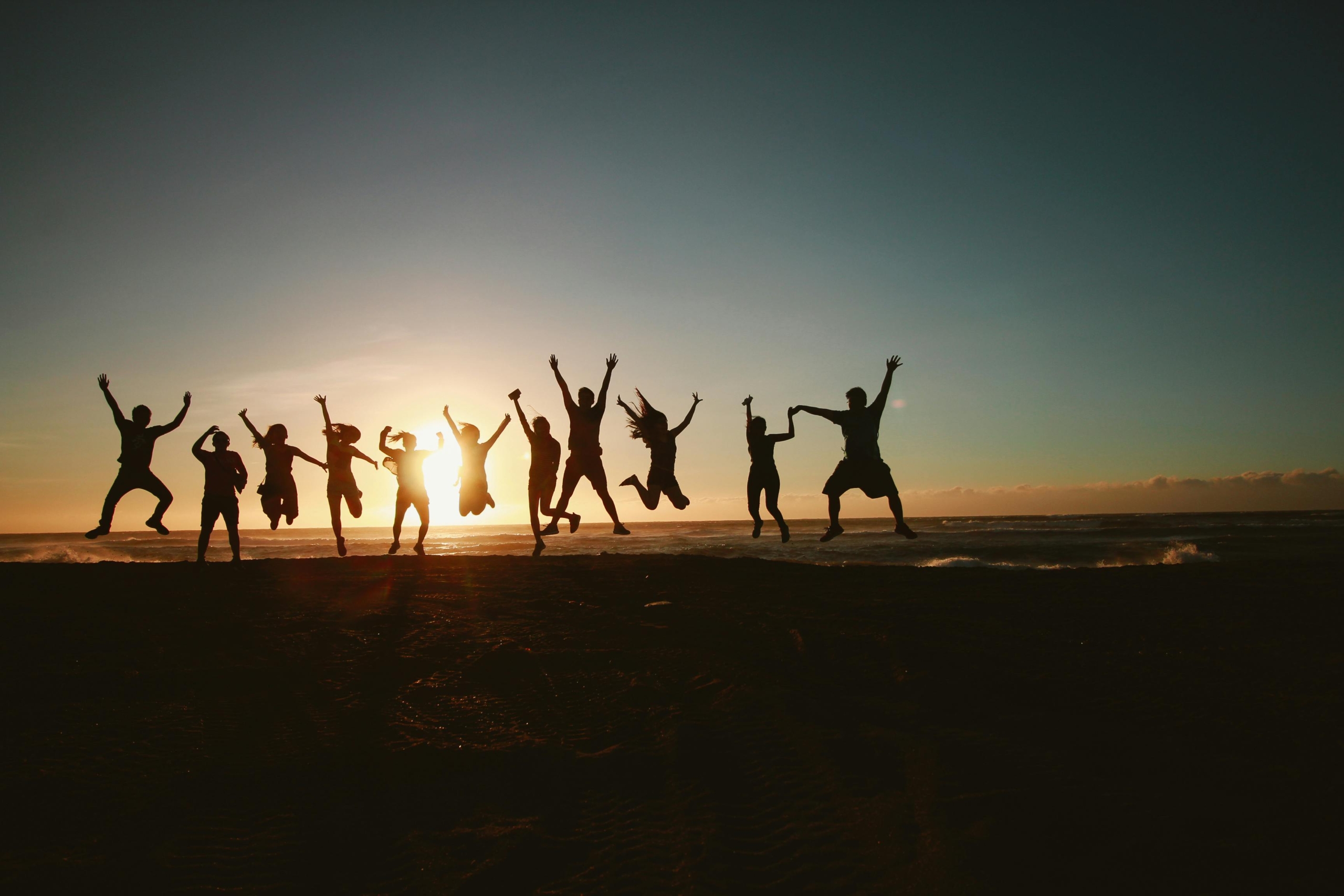 A silhouette of a group of people captured mid-jump on the beach at sunset.