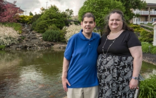 Nick and Rachel smiling at the camera with a scenic pond in the background.