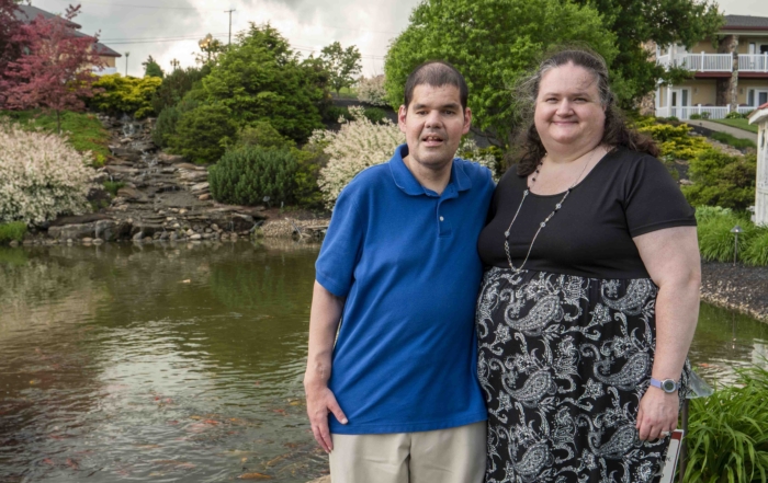 Nick and Rachel smiling at the camera with a scenic pond in the background.