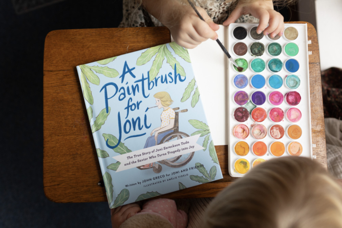 A Paintbrush for Joni book next to children painting with watercolors