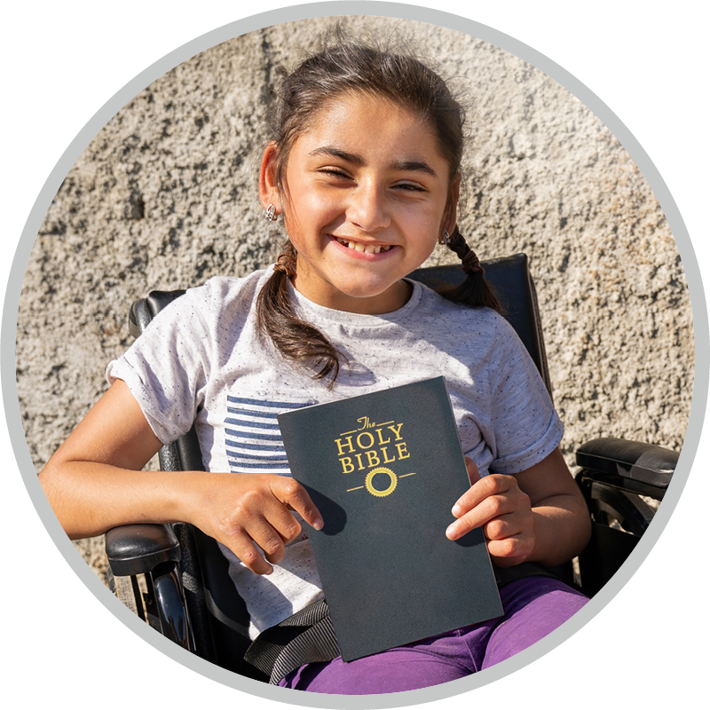 A little girl in a wheelchair holding a Bible.