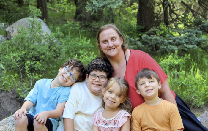 Tara with Max, Matthew, Hailie, and Mikey smiling together outdoors in front of green bushes