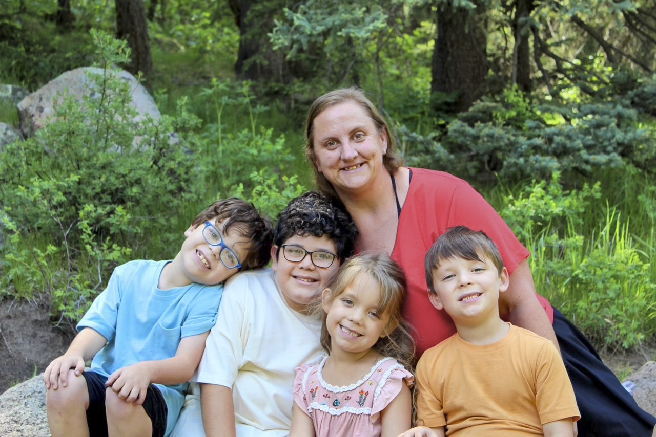 Tara with Max, Matthew, Hailie, and Mikey smiling together outdoors in front of green bushes