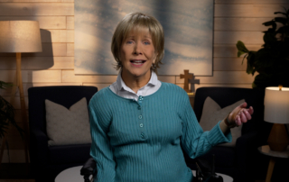 Joni Eareckson Tada smiling, wearing a long-sleeve in a cozy living room.
