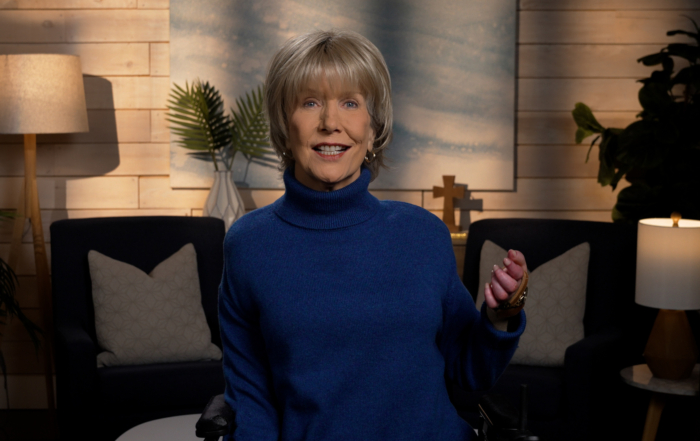 Joni Eareckson Tada smiling, wearing a long-sleeve turtle neck in a cozy living room.