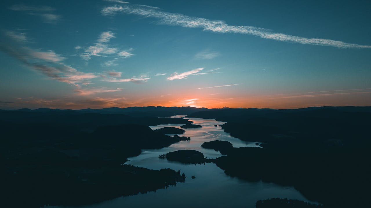 Aerial view of a winding river beside a dense forest at sunset, with golden-hour light casting a warm glow and creating a peaceful, reflective atmosphere.