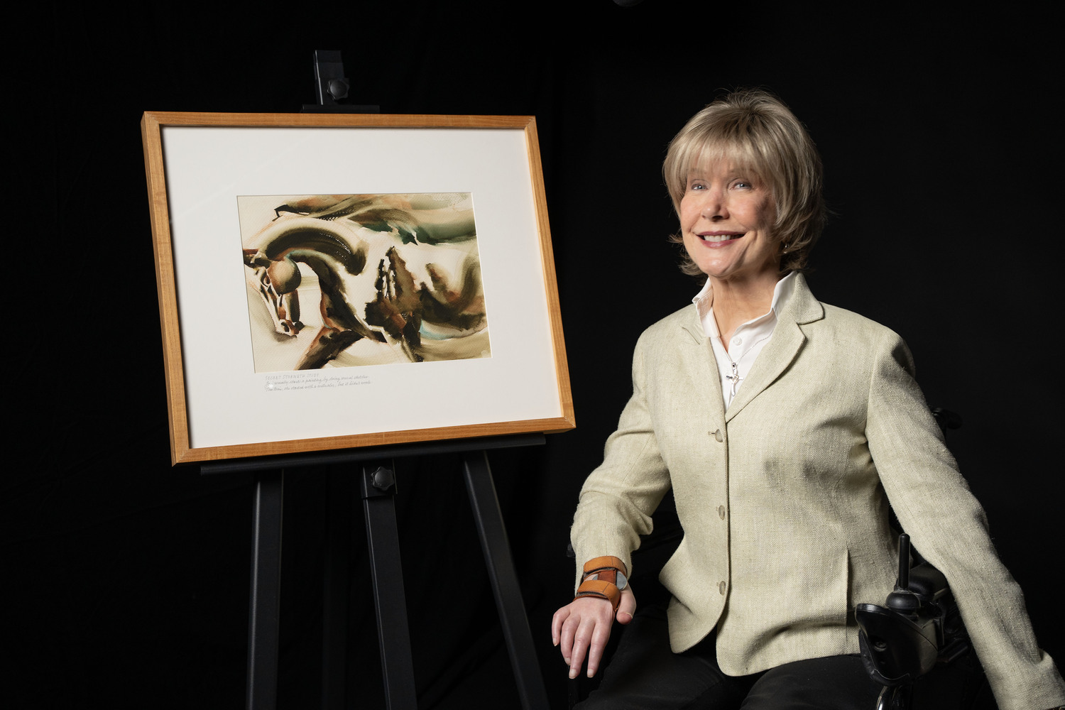Joni sitting on the left in her wheelchair next to her painting of a horse in motion.