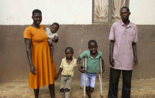 Angello Lukabwe stands with crutches and smiles with his two siblings and his parents for the camera.