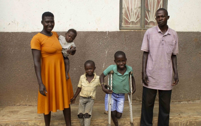Angello Lukabwe stands with crutches and smiles with his two siblings and his parents for the camera.