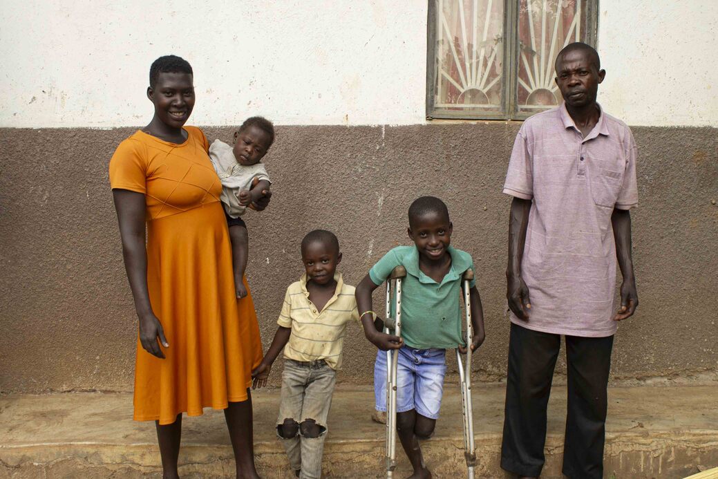 Angello Lukabwe stands with crutches and smiles with his two siblings and his parents for the camera.