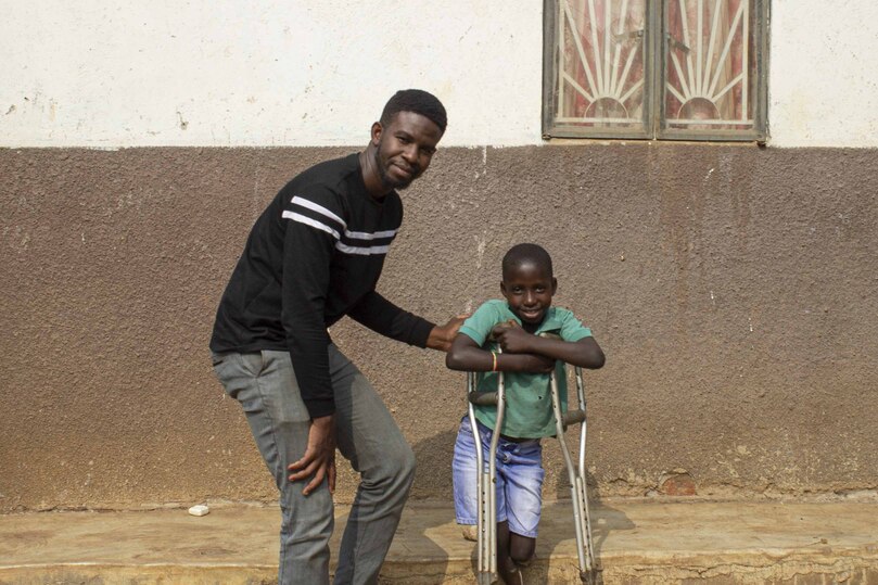 Angello Lukabwe stands on his crutches next to another man and both smile for the camera.