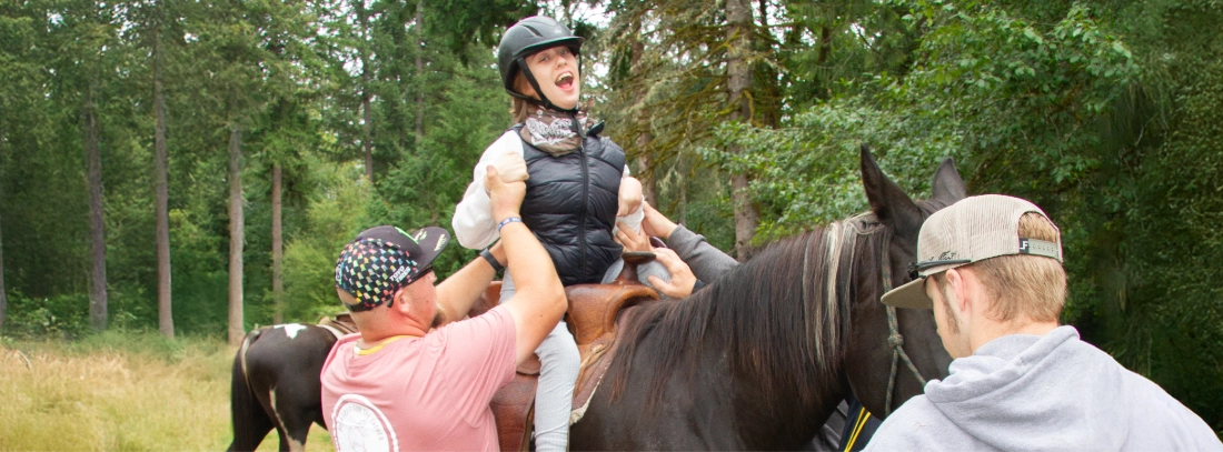 A camper on a dark-brown horse with volunteers assisting