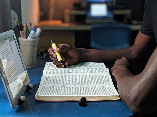A person highlighting the Bible in front of a screen on an iPad.