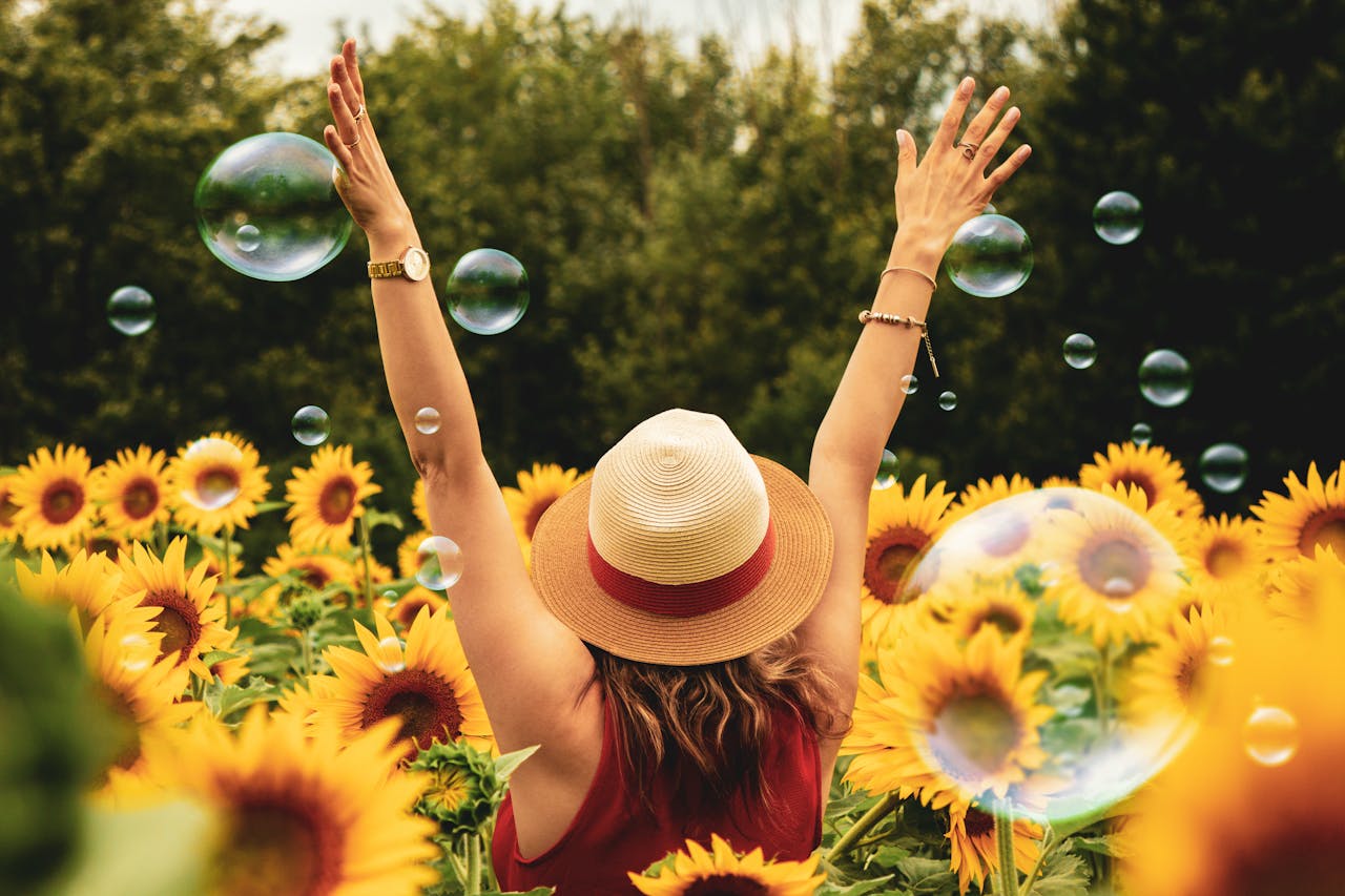 A girl raising both hands, enjoying the moment while surrounded by sunflowers and floating bubbles.