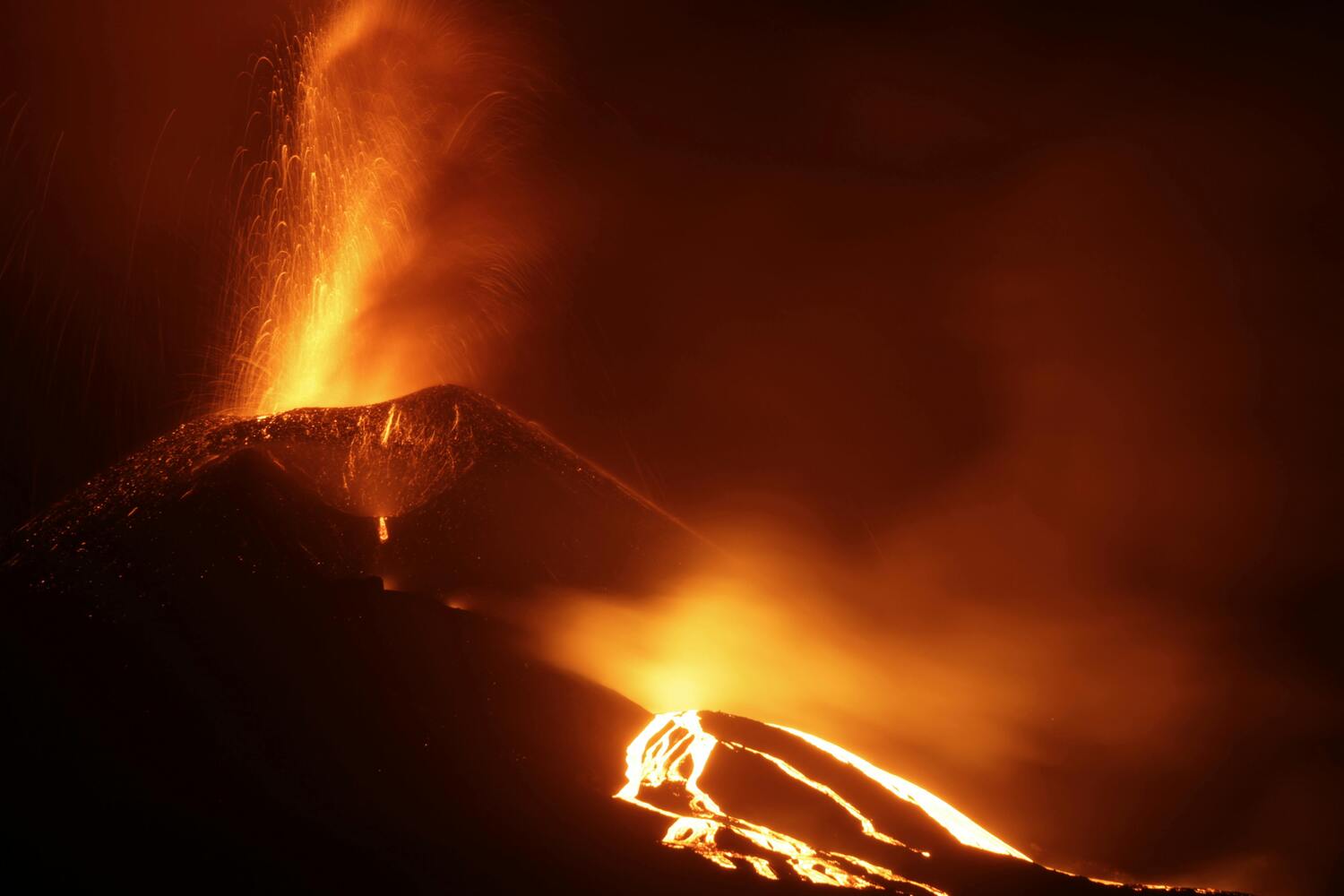 A glowing volcano erupting at night, with bright orange lava flowing down its sides and sparks shooting into the dark sky.