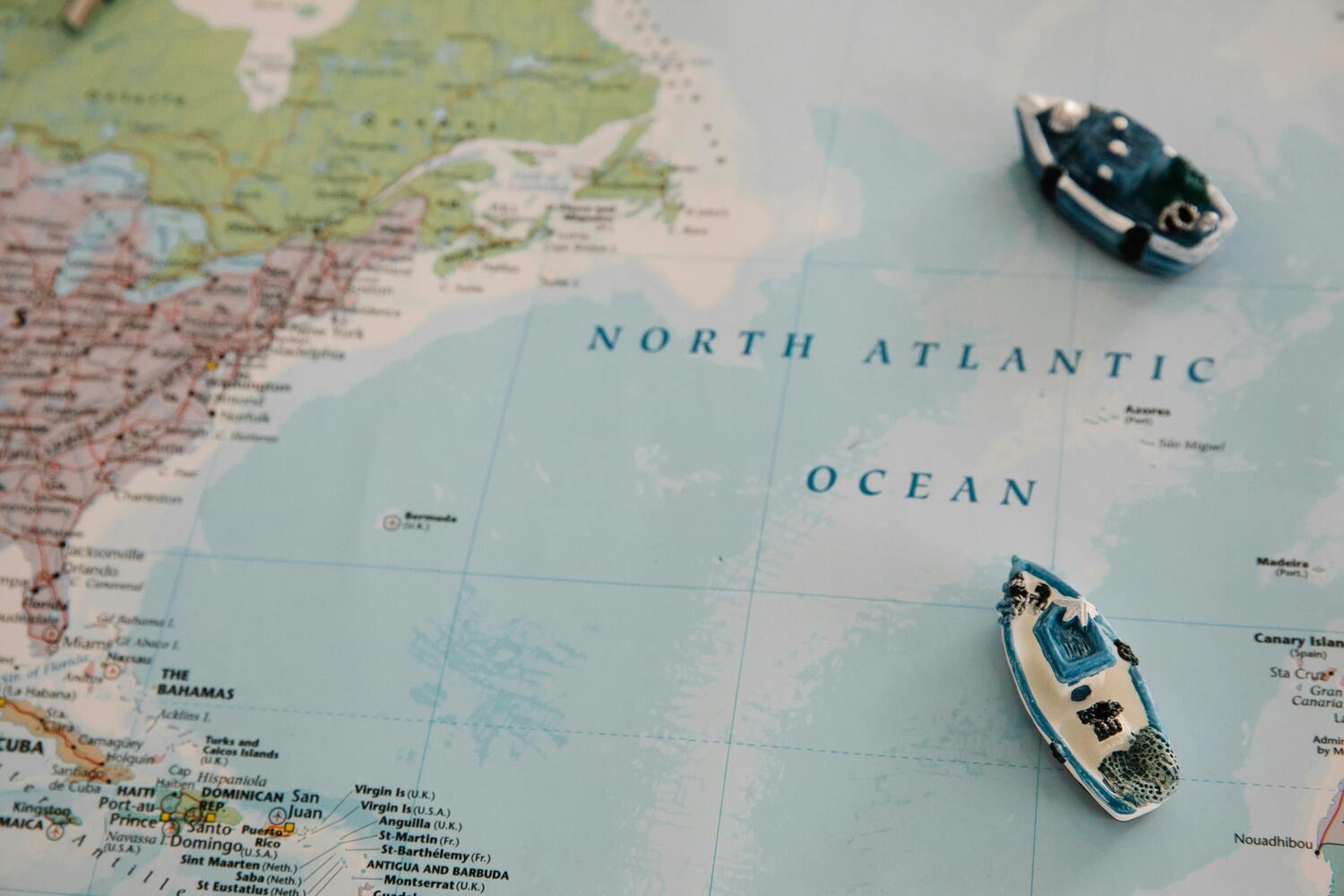 A photo of a physical world map with two small white and blue toy boats placed on the North Atlantic Ocean.