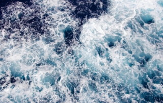 A top-down view of ocean water with white foam and swirling shades of deep blue and turquoise.
