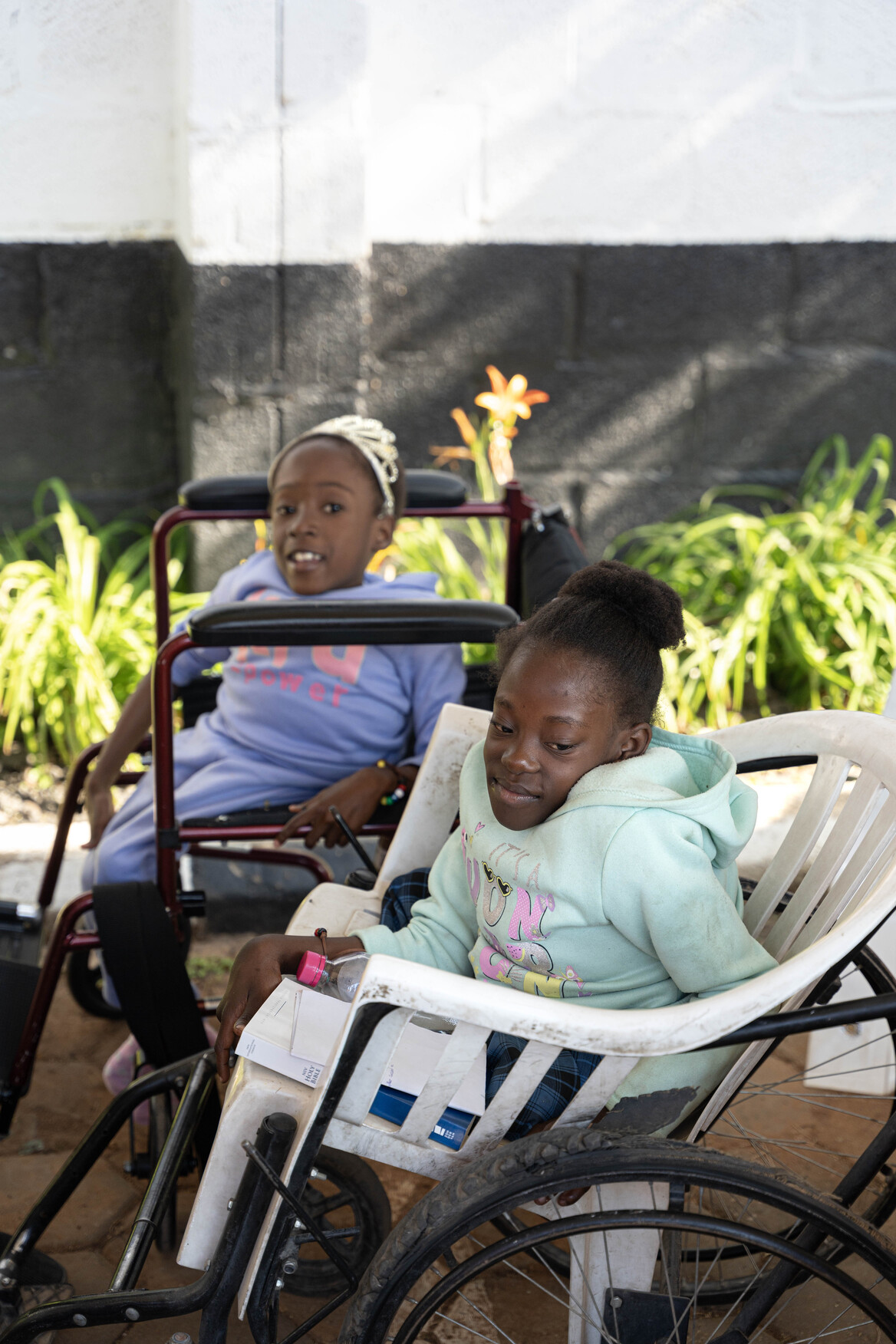 Chichi and Diana sit next to each other, patiently waiting for new wheelchairs.