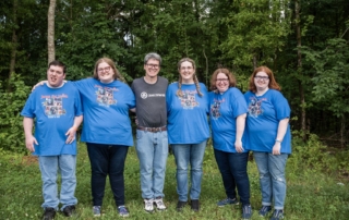 The whole Clayton family standing together outdoors, smiling and posing for the camera, surrounded by greenery and showing a warm, happy family moment.