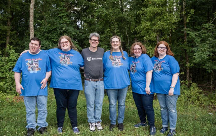 The whole Clayton family standing together outdoors, smiling and posing for the camera, surrounded by greenery and showing a warm, happy family moment.