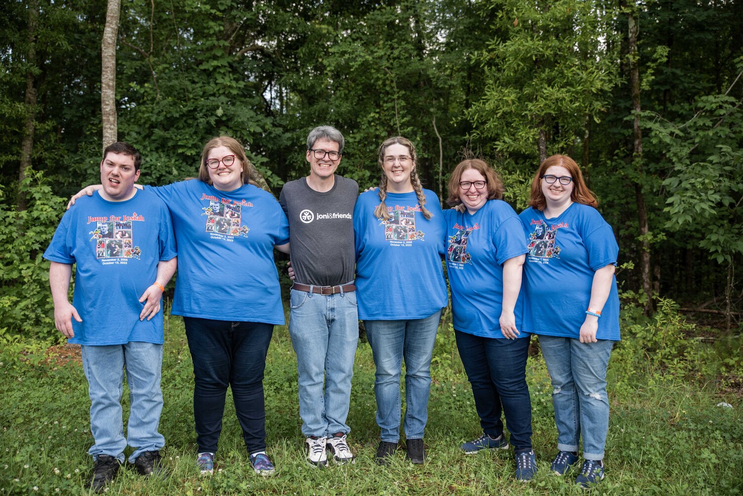 The whole Clayton family standing together outdoors, smiling and posing for the camera, surrounded by greenery and showing a warm, happy family moment.