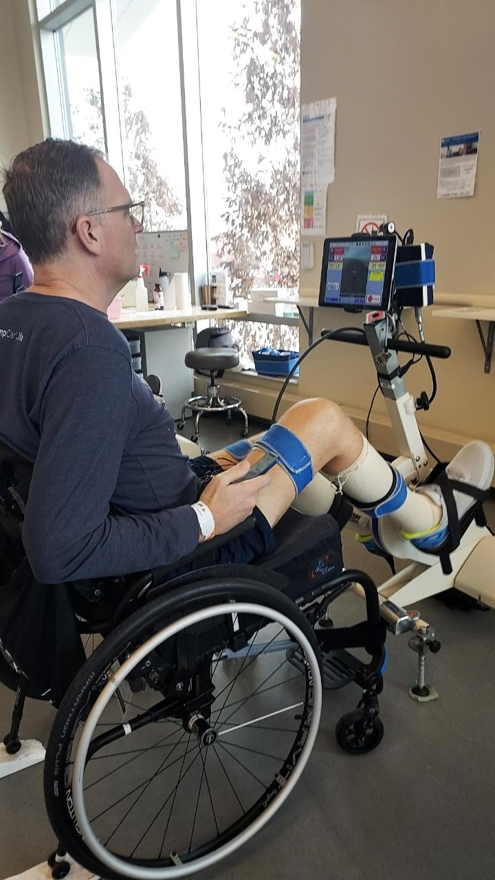 Jason Kolb in front of a leg exercise machine, with his legs secured to it.