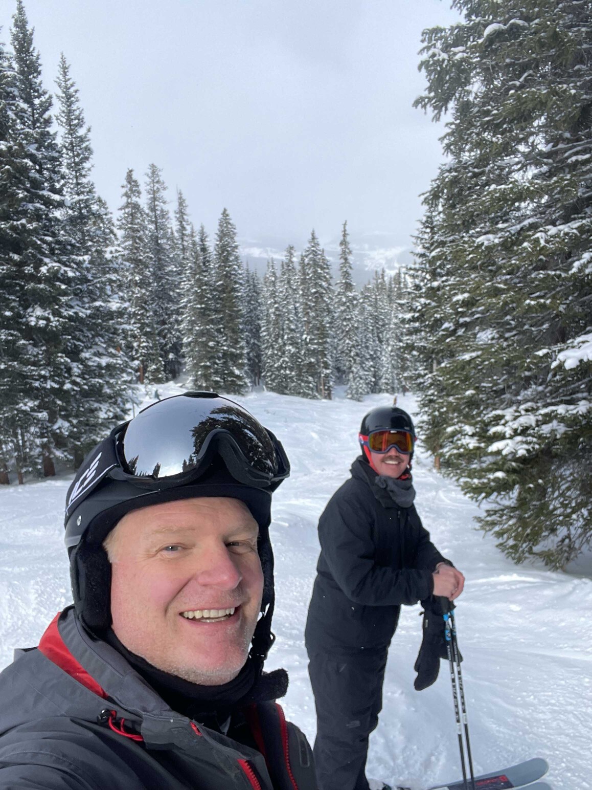 Jason Kolb skiing with another man. Both are smiling for the camera.