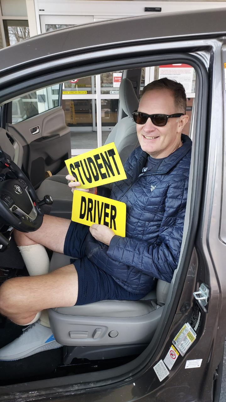 Jason Kolb inside a car holding a sign that says "Student Driver"