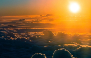 A vibrant sunrise above a sea of fluffy clouds, with golden light spilling across the sky and casting warm orange and yellow hues on the cloud tops.