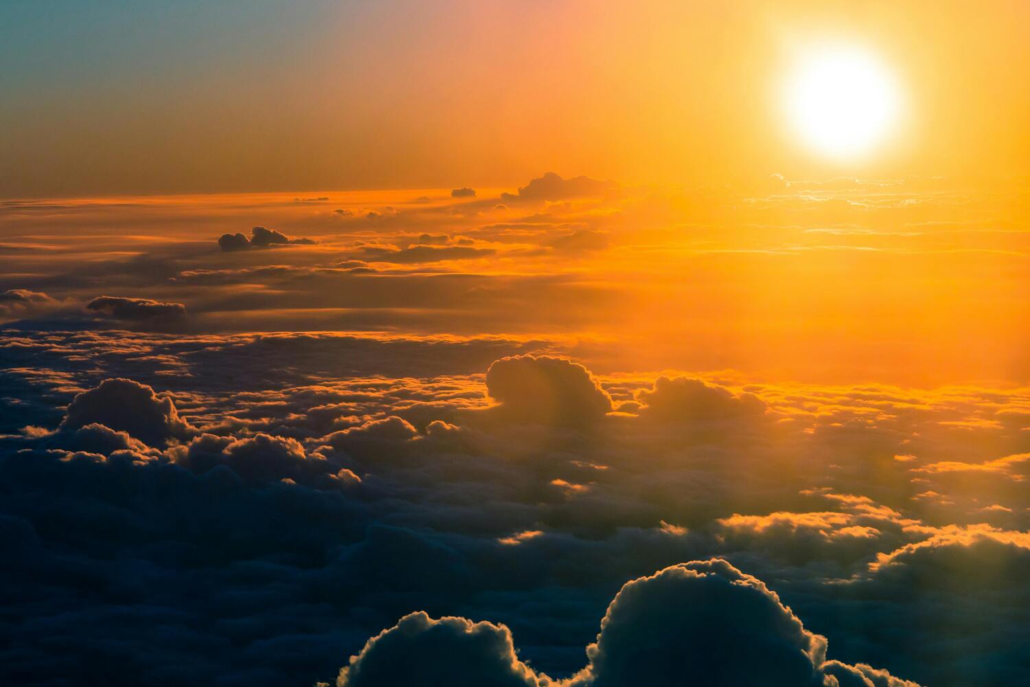 A vibrant sunrise above a sea of fluffy clouds, with golden light spilling across the sky and casting warm orange and yellow hues on the cloud tops.