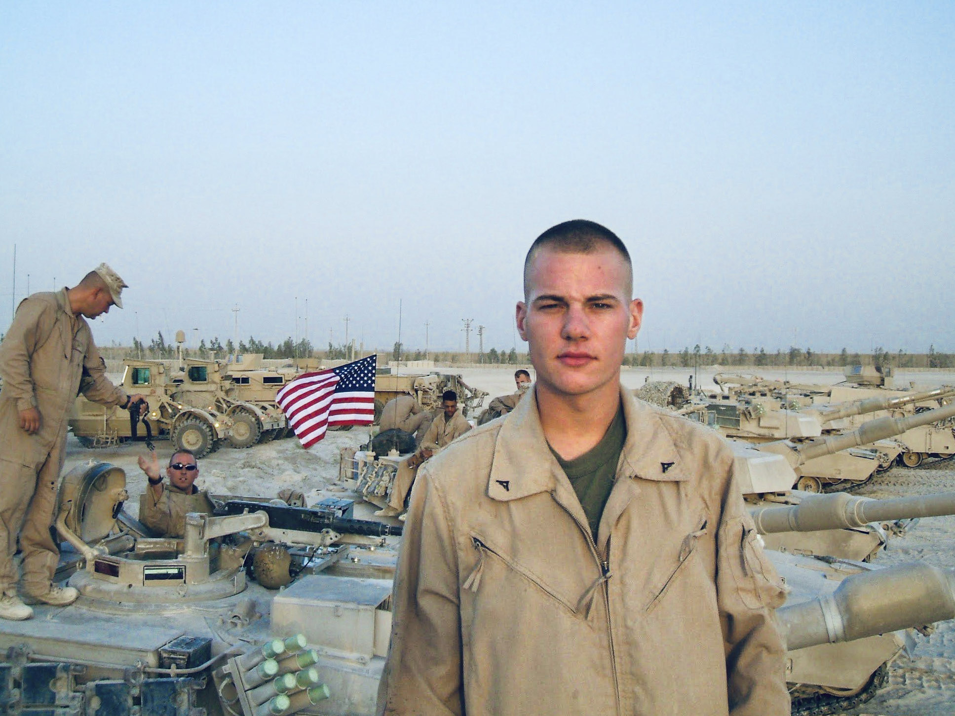 Mark Stallion looks at the camera with tanks and fellow soldiers in the background.