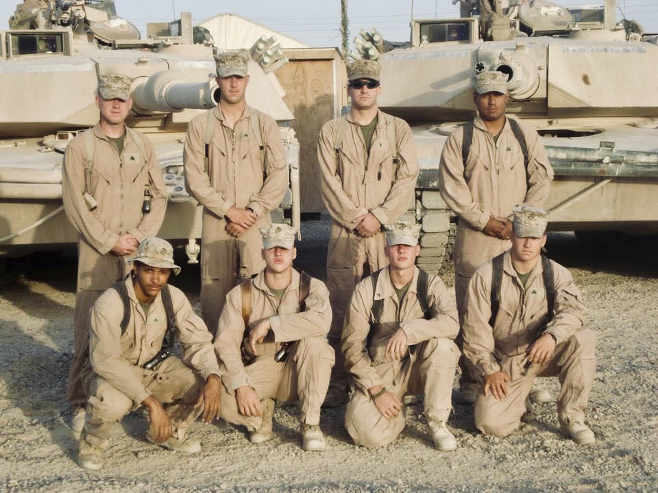 Mark Stallion and other soldiers pose for the camera with tanks in the background.