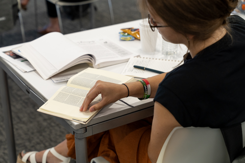 A young student with glasses intently reading an open Bible with the Beyond Suffering book next to it on a table.